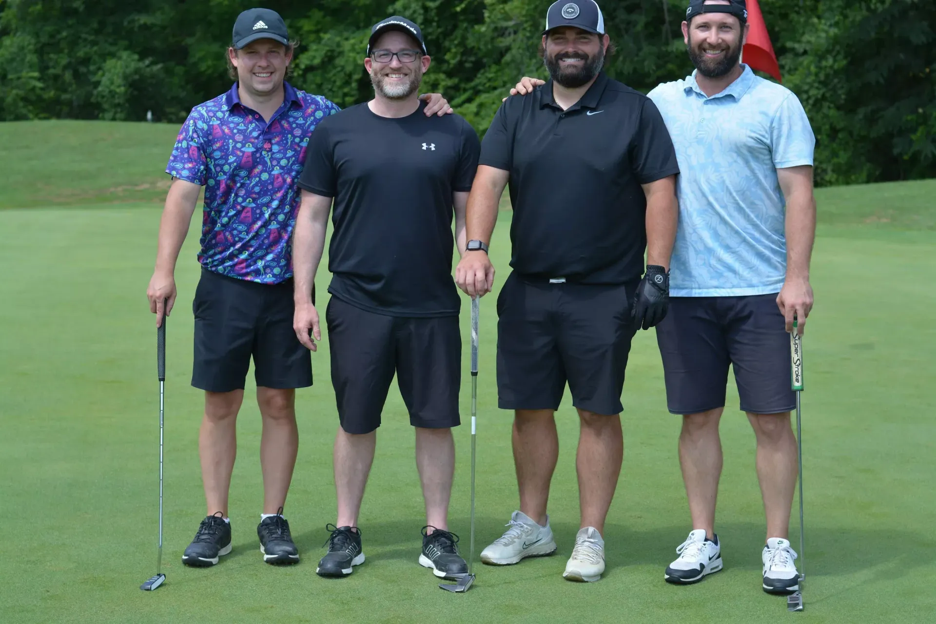 Four golfers standing on a green, posing with clubs under a cloudy sky.