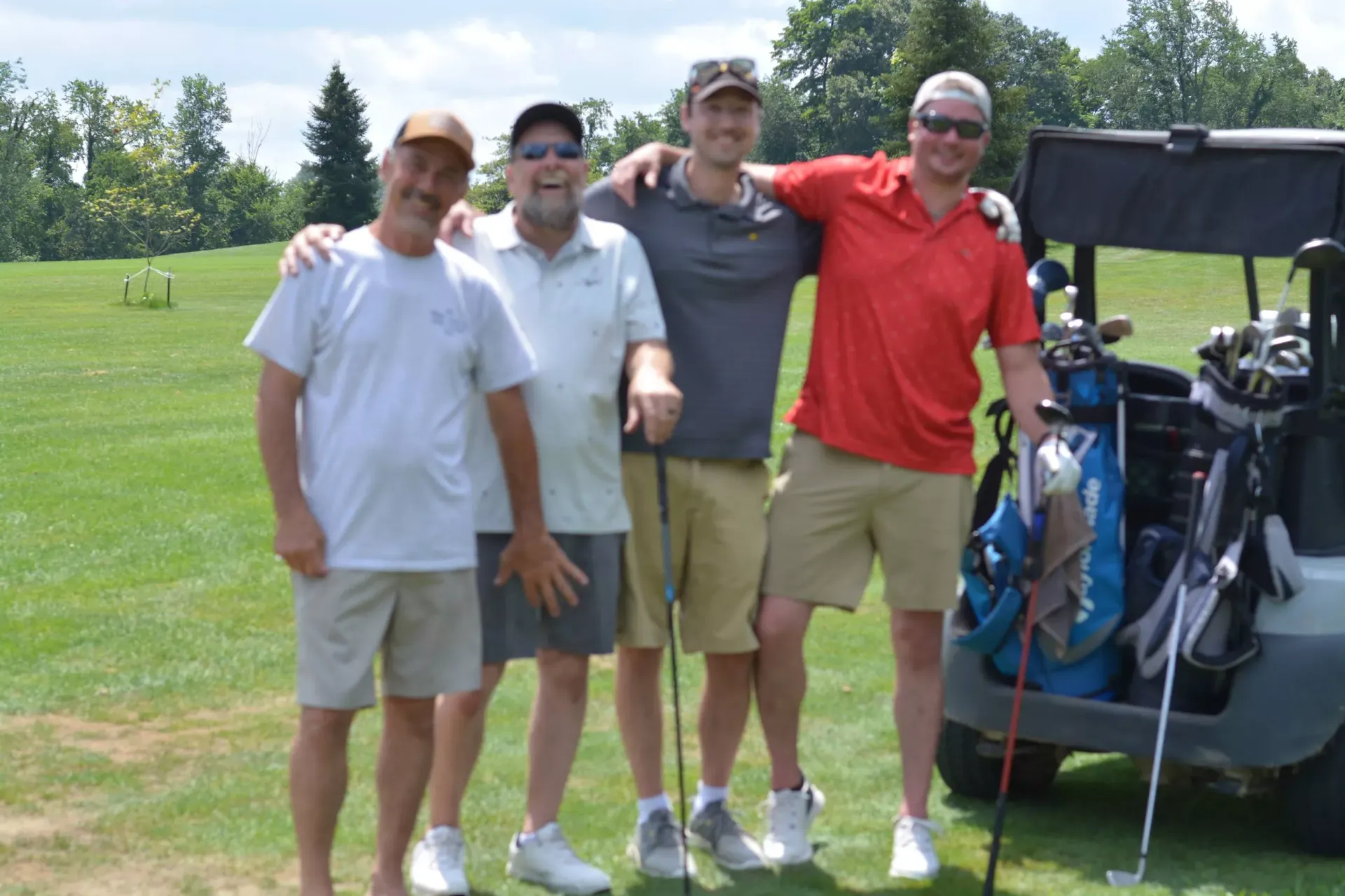 Four golfers standing together on a sunny course beside a golf cart and bags