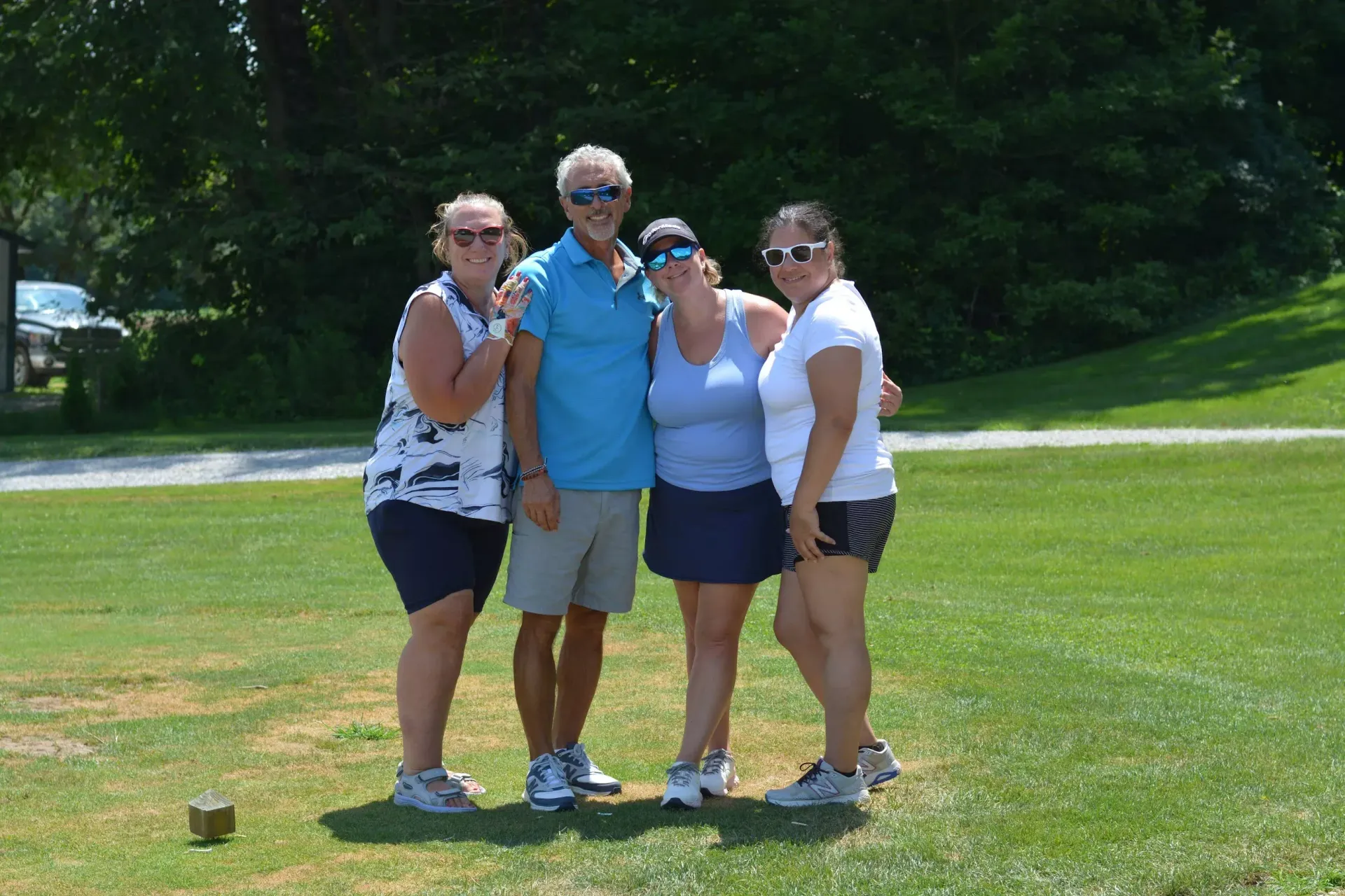 Four friends posing together on a sunny golf course, smiling and standing close on the grass.