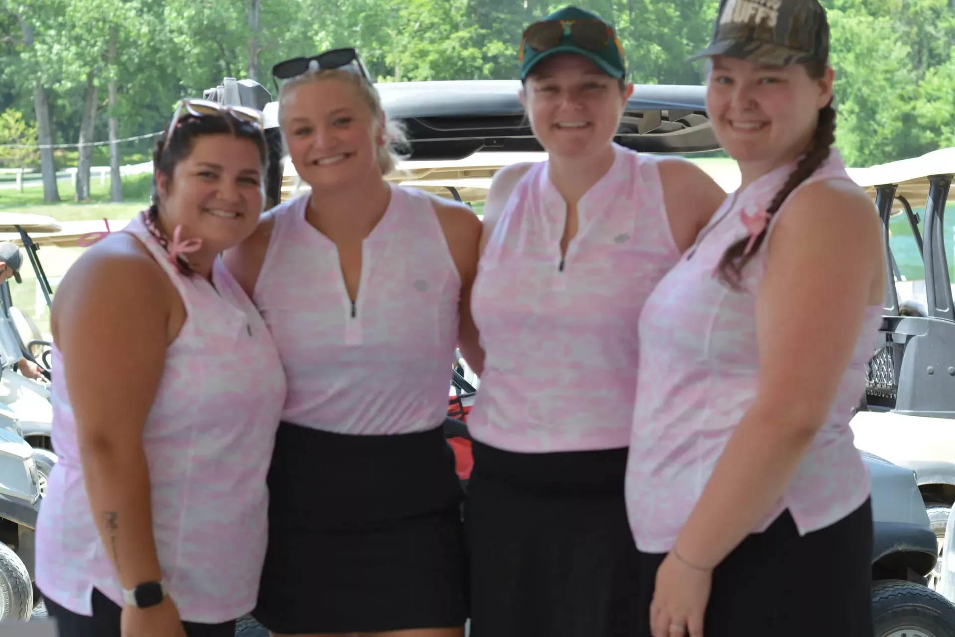 Four people in matching pink shirts and black skirts standing together outdoors, smiling.