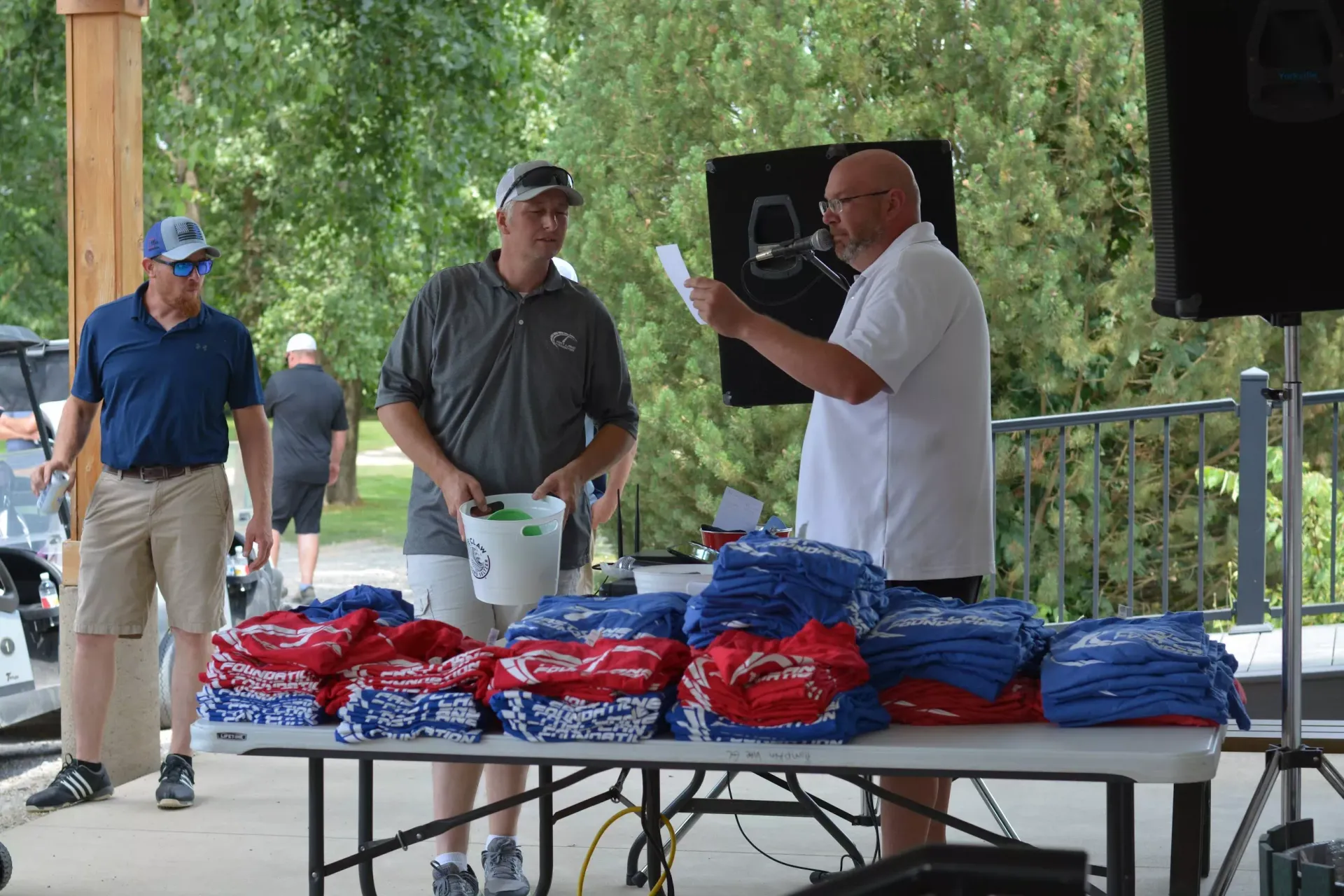 Volunteers at an outdoor table handing out red and blue shirts at a park pavilion