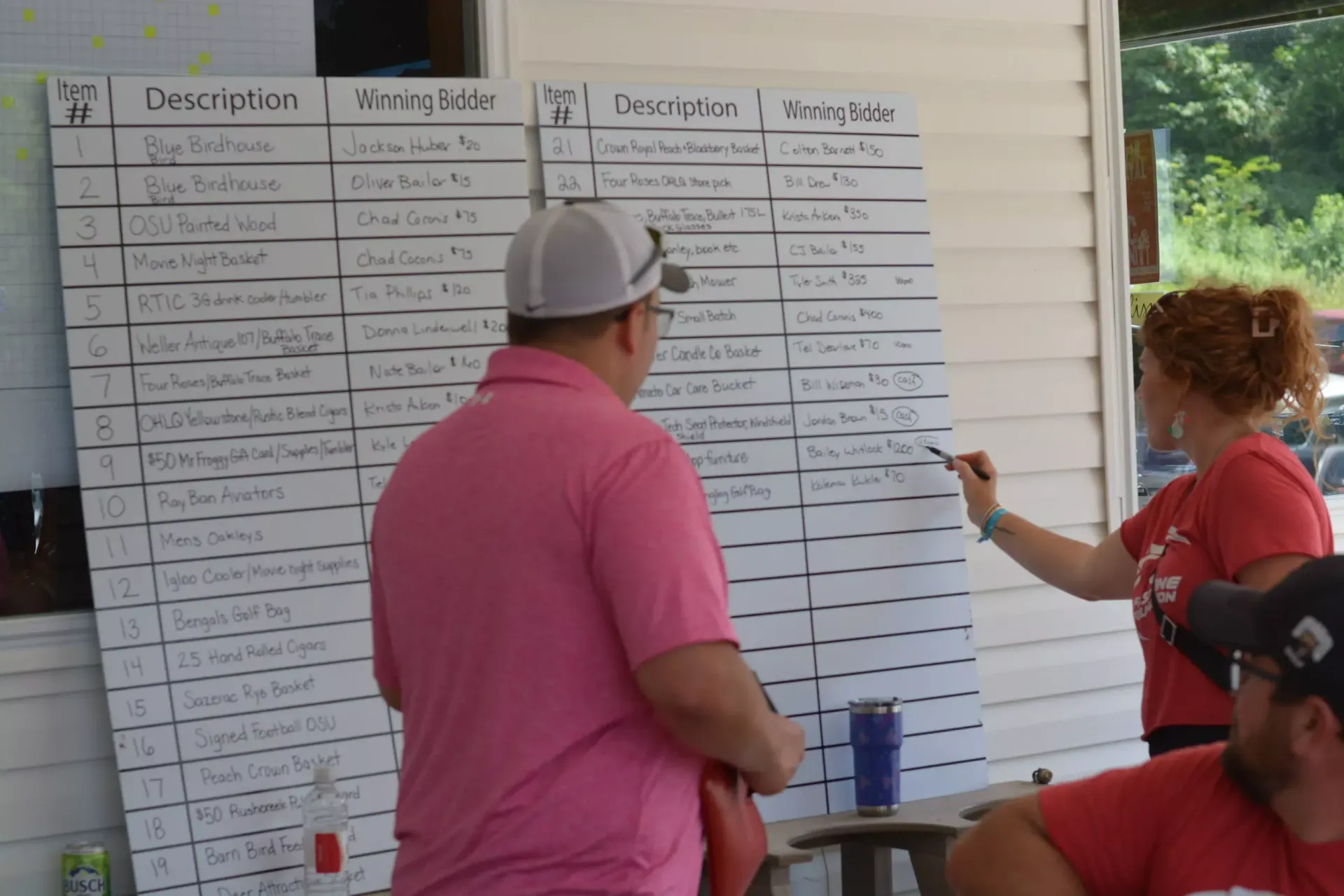 People reviewing a large event schedule board outdoors under a pavilion.