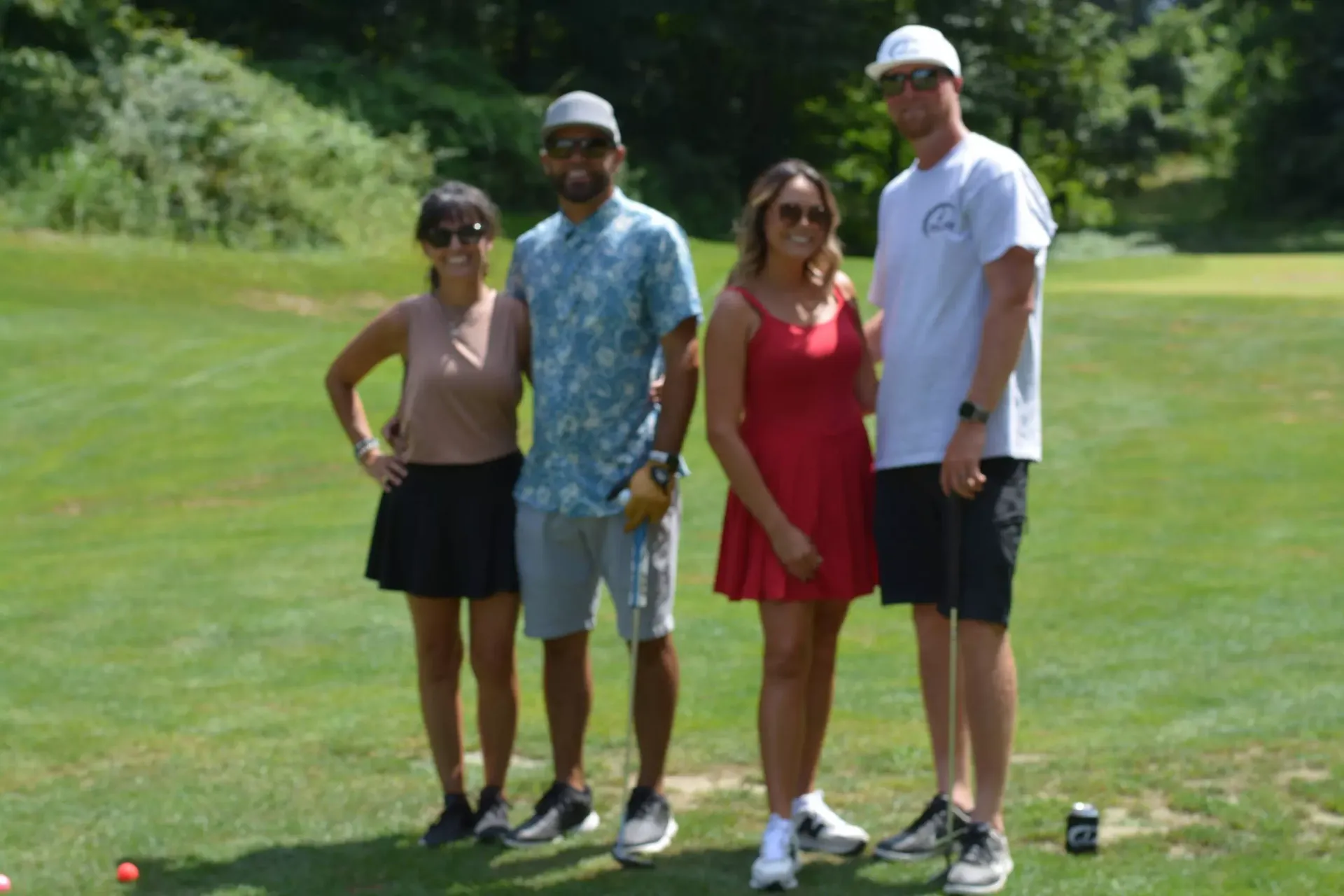 Four people standing on a golf course, posing together in casual summer clothes