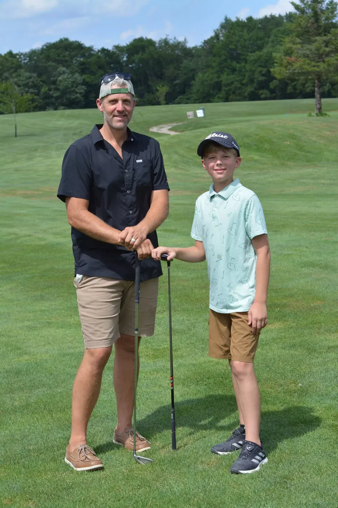 Two golfers standing on a green fairway, holding clubs and smiling at the camera.