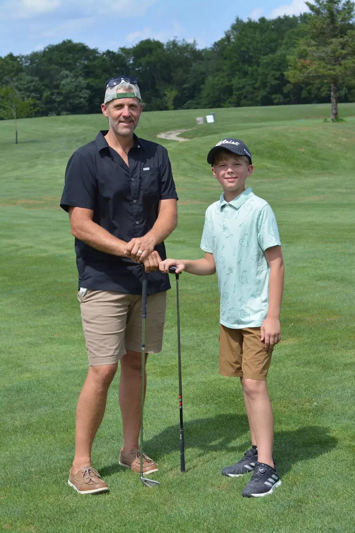 Two golfers standing on a green fairway, smiling and holding a golf club together.