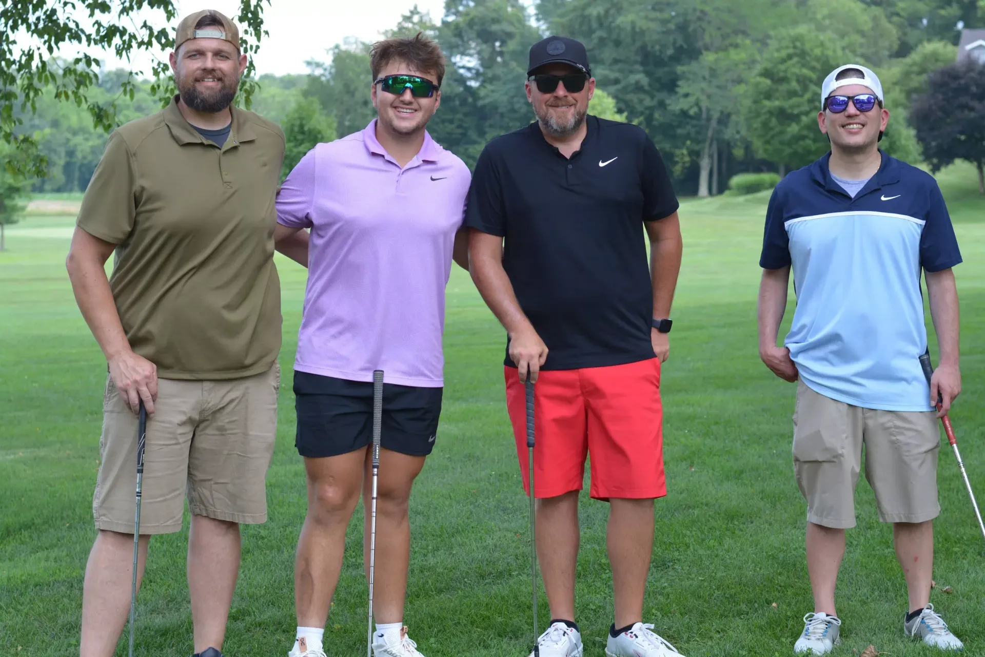 Four people standing outdoors on grass, smiling in casual golf attire.