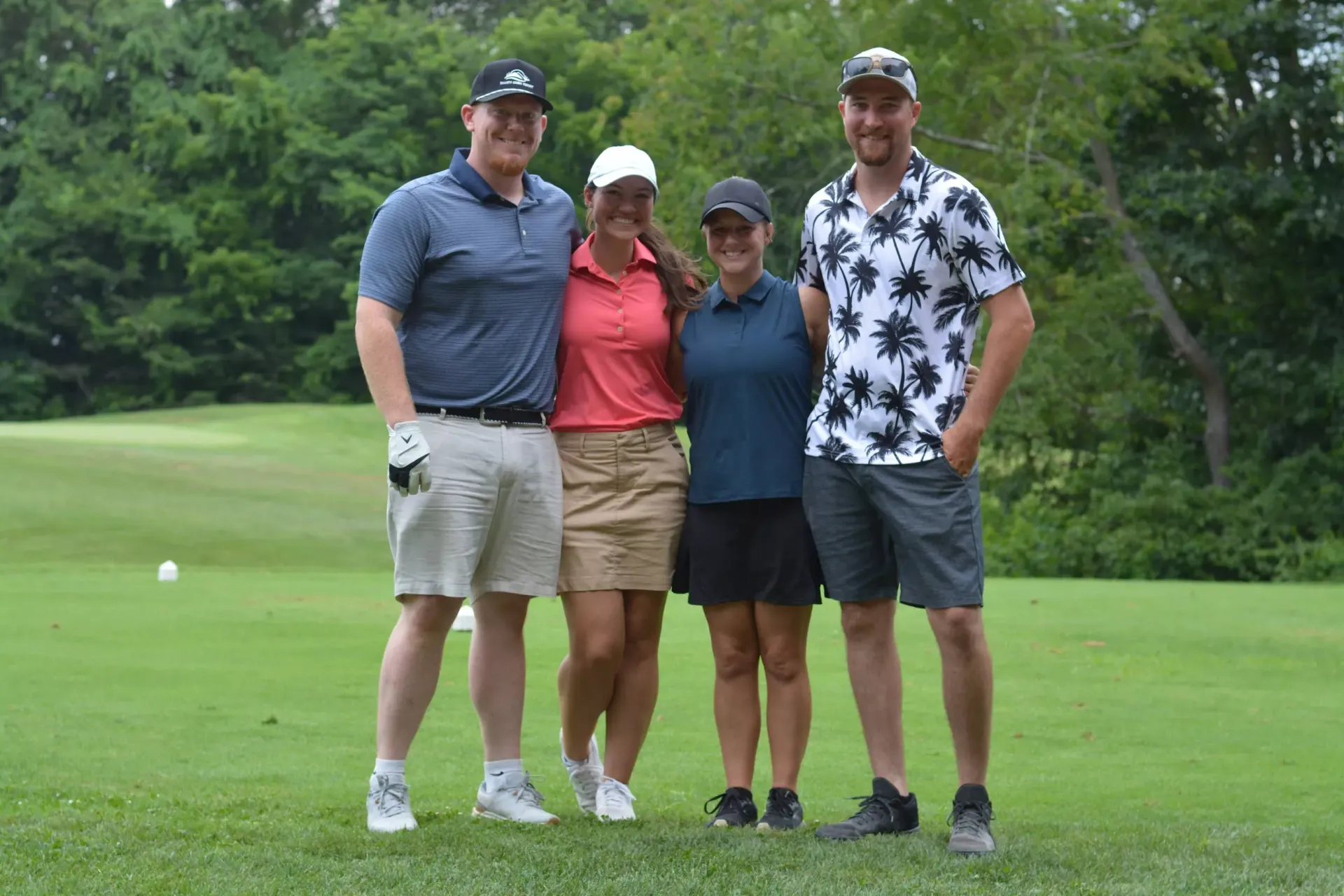 Four people standing together on a grassy golf course, posing for a photo.