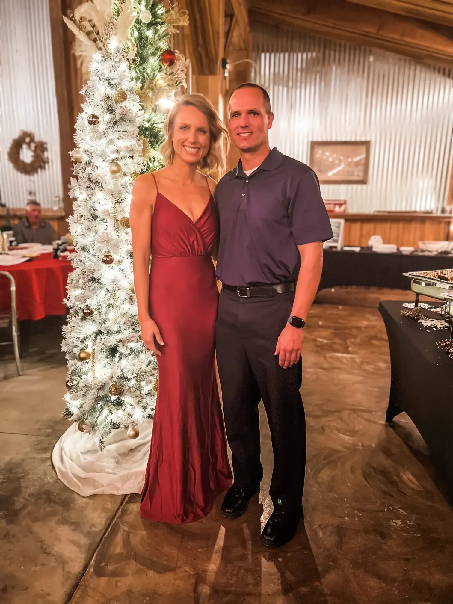 Couple posing at an elegant holiday event beside a white-lit Christmas tree