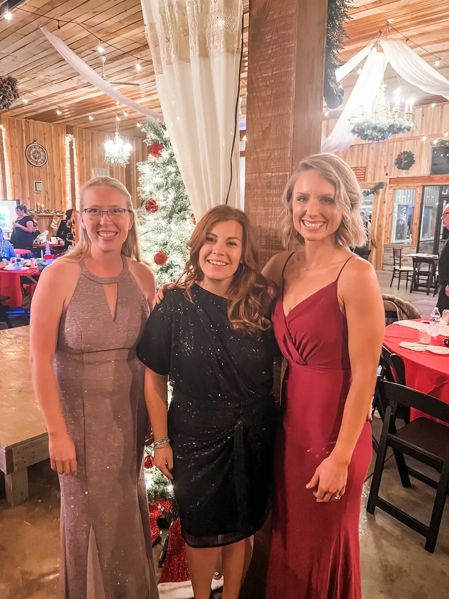 Three women posing at a festive indoor event with holiday lights and decorations