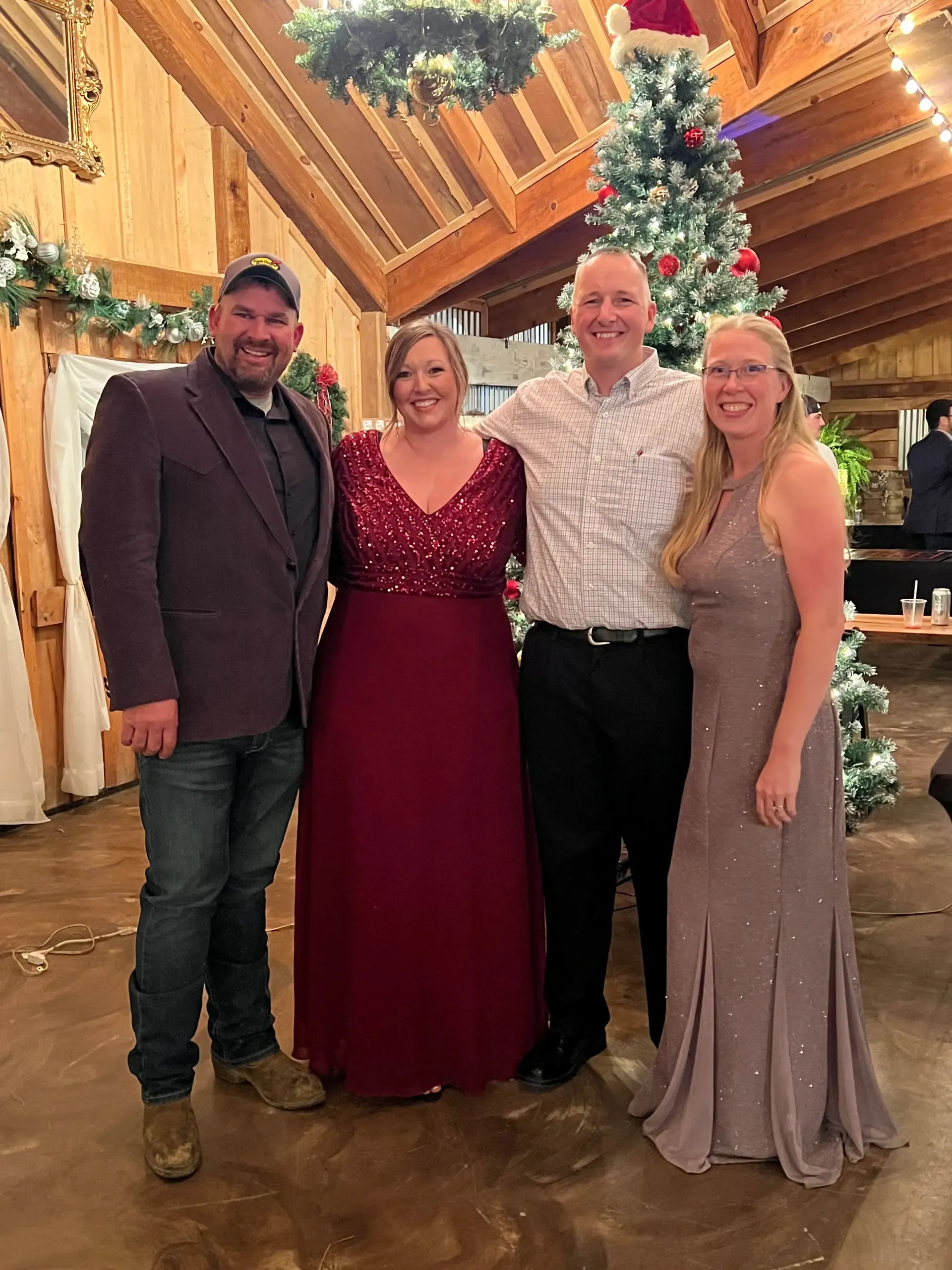 Four people posing in festive attire in a decorated wooden lodge with a Christmas tree.
