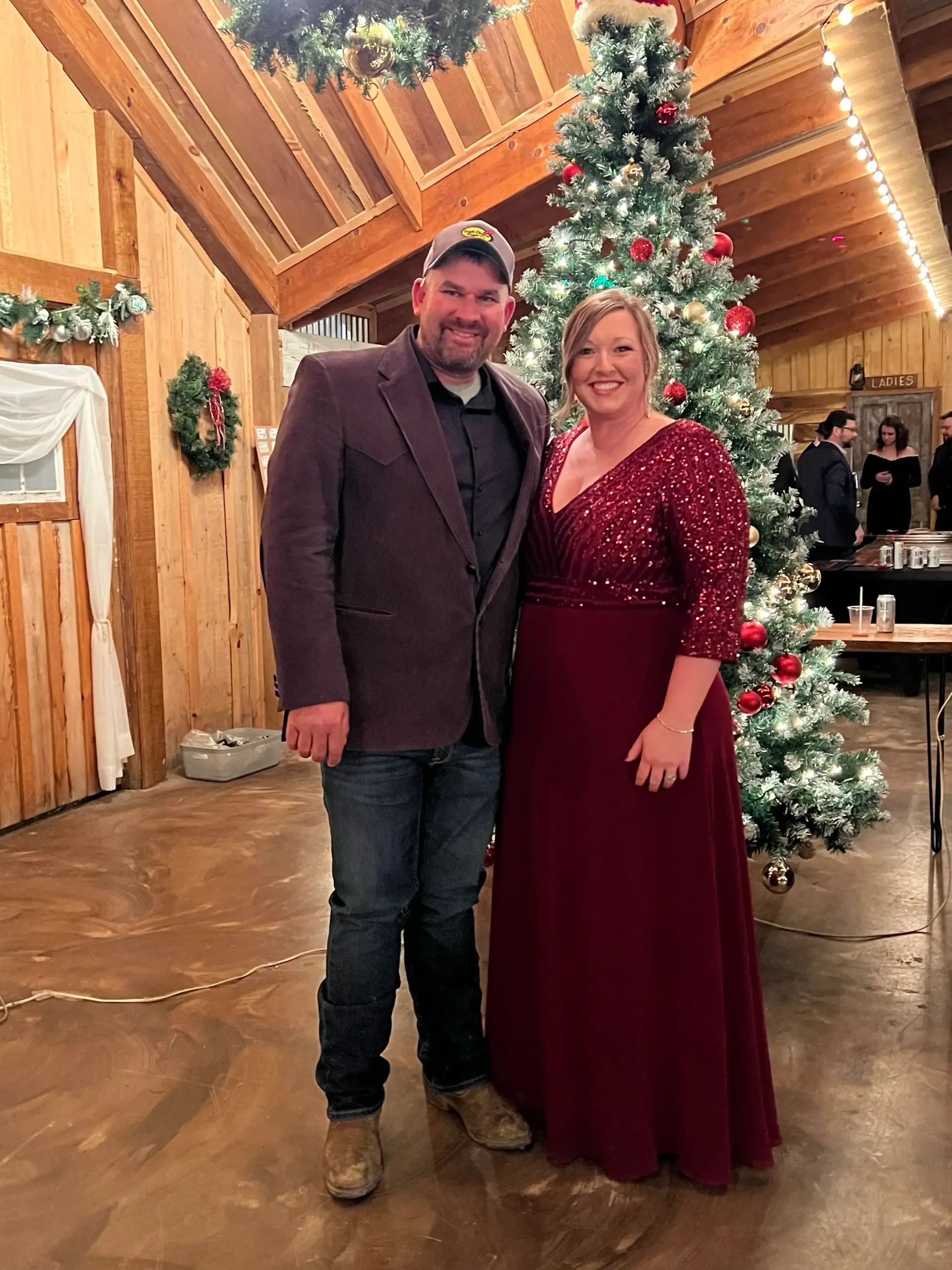 Couple posing in front of a decorated Christmas tree inside a rustic, wood-paneled venue.