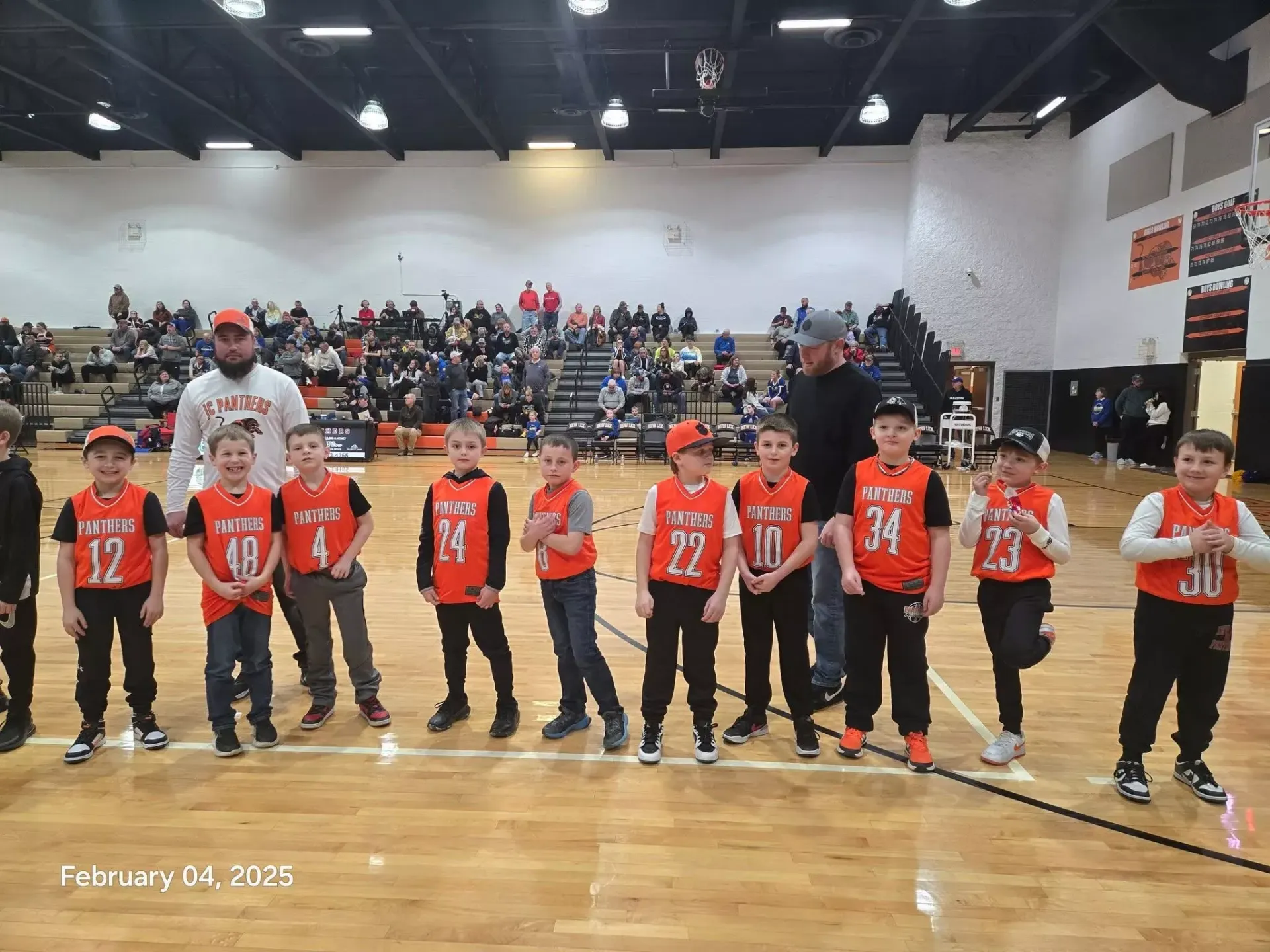 Youth basketball team lined up on a gym court in orange jerseys during a game event.