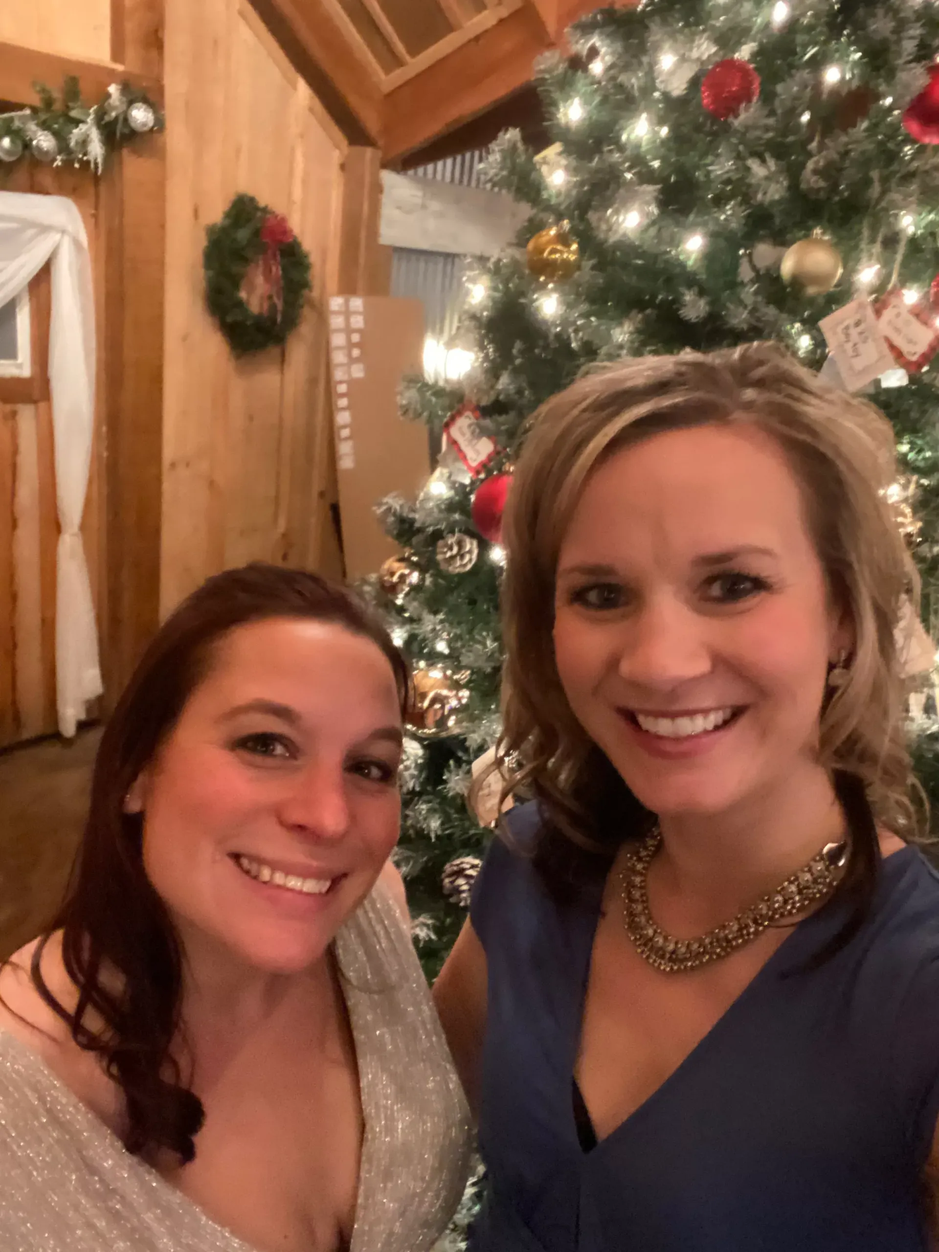 Two women smiling beside a lit Christmas tree and holiday decorations