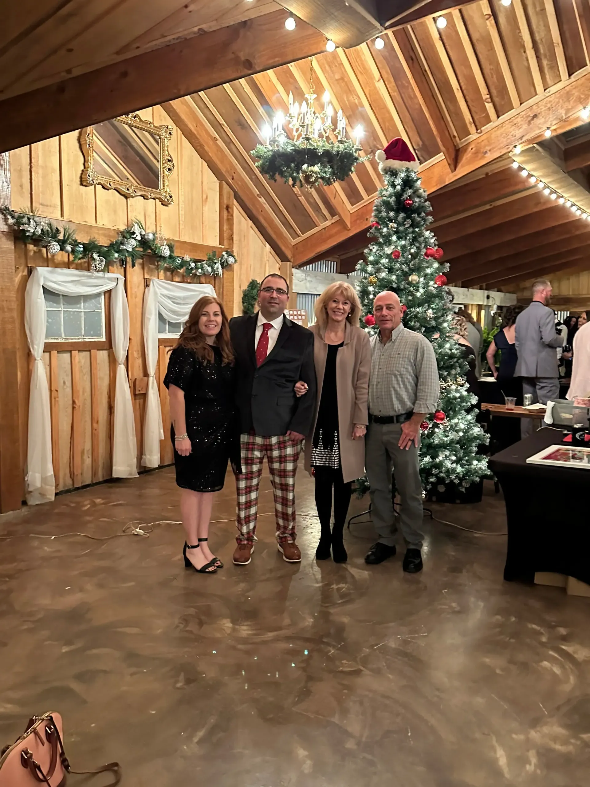 Four people posing in a decorated rustic hall beside a lit Christmas tree.
