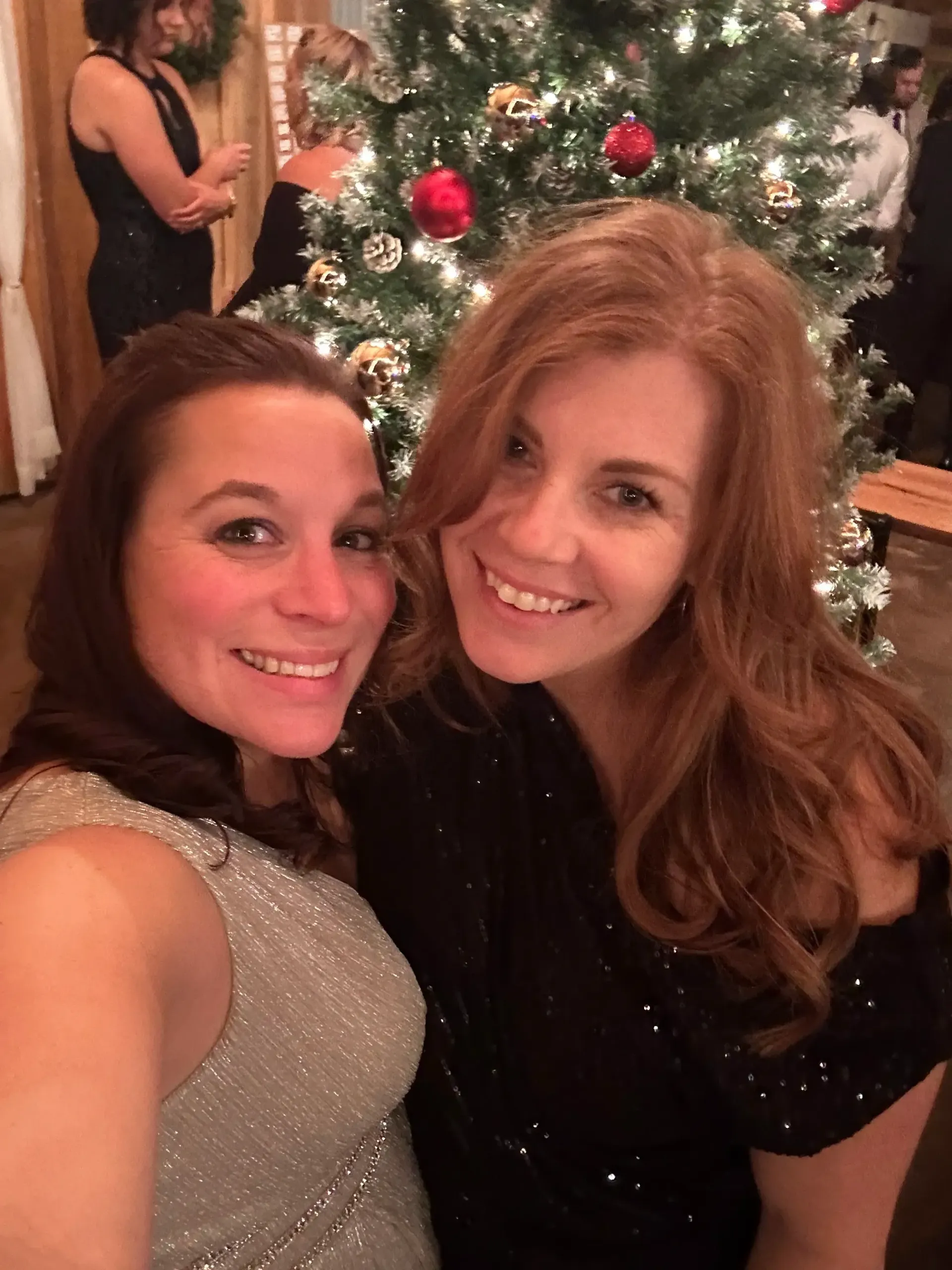 Two women smiling for a selfie in front of a decorated Christmas tree