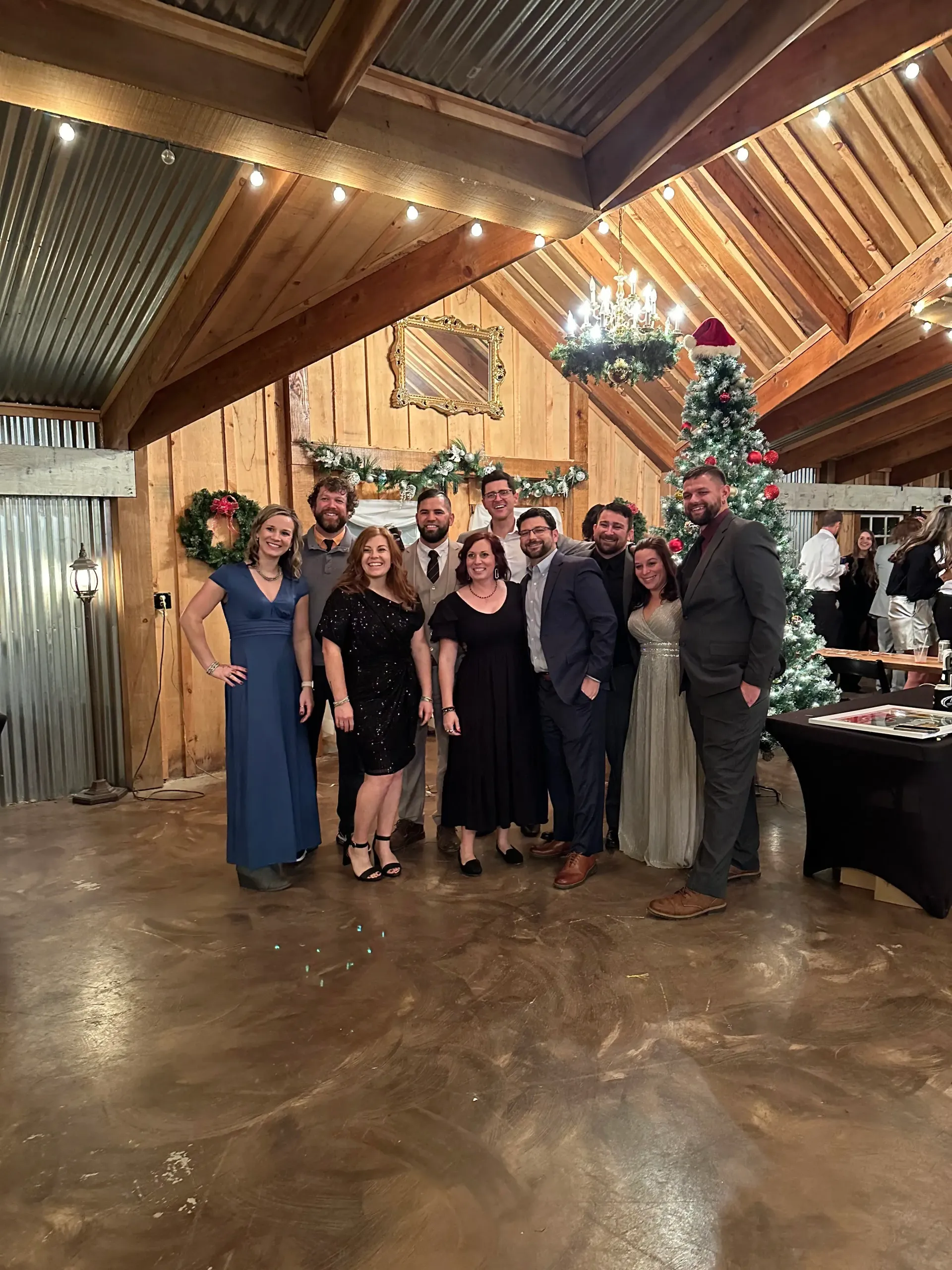 Group posing at a holiday party in a rustic venue with a decorated Christmas tree and warm string lights.