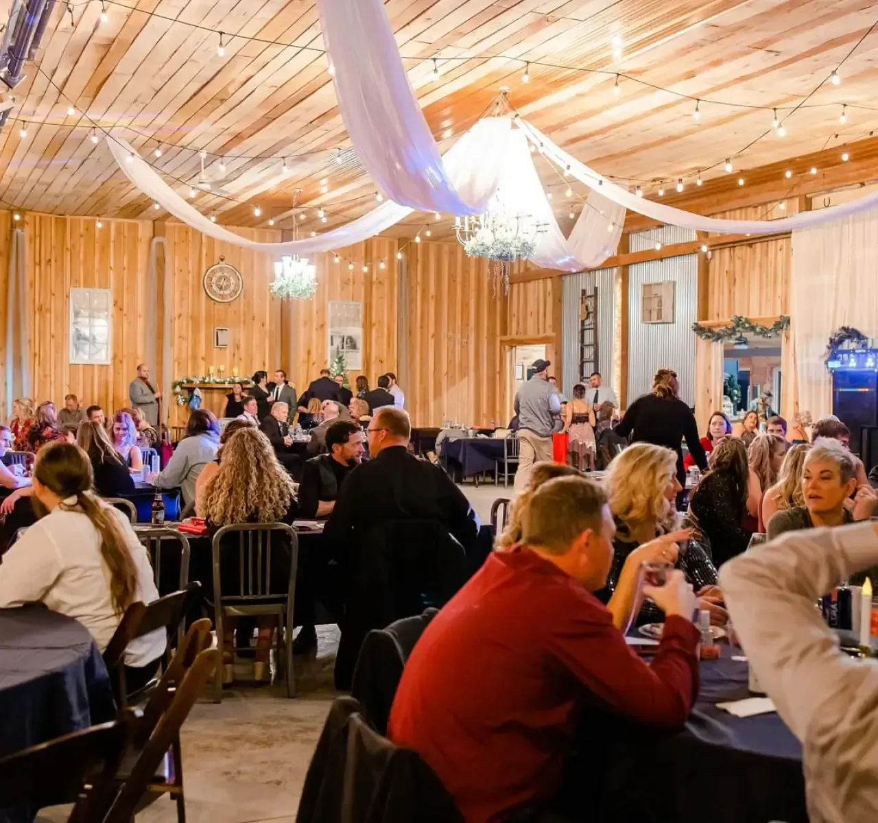 Guests seated at tables in a warmly lit wooden banquet hall with draped fabric ceiling decor