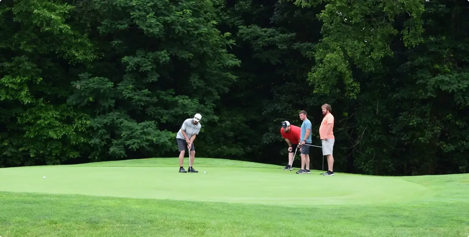 Golfers on a green putting surface with one person preparing a putt and others watching nearby