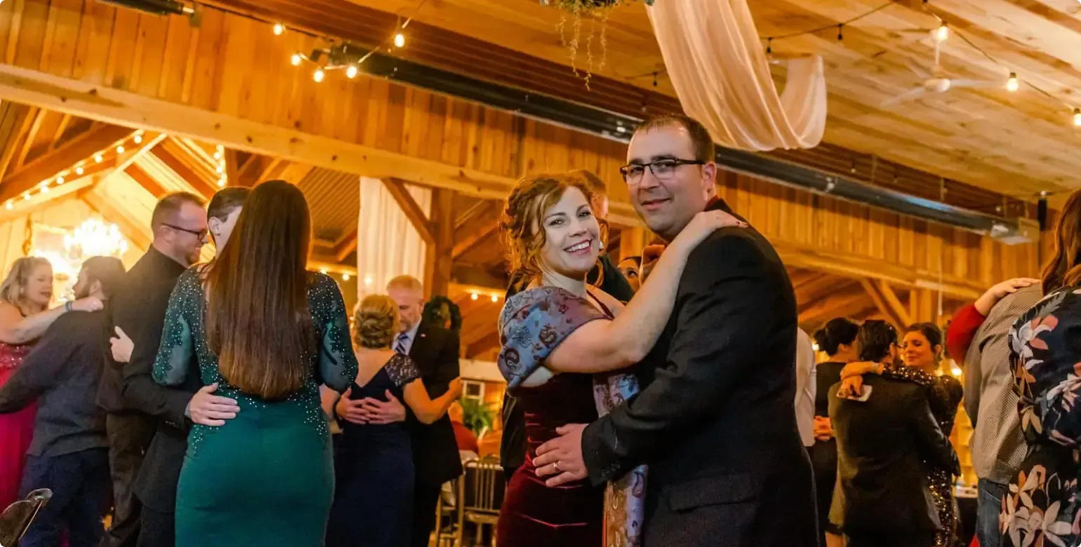 Couple dancing at a warmly lit indoor reception with guests mingling in the background