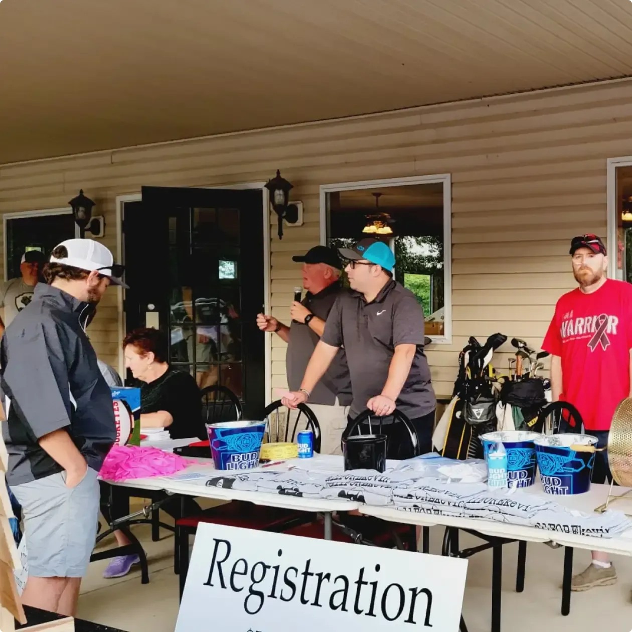 People at a registration table under a porch, with a sign and blue buckets.