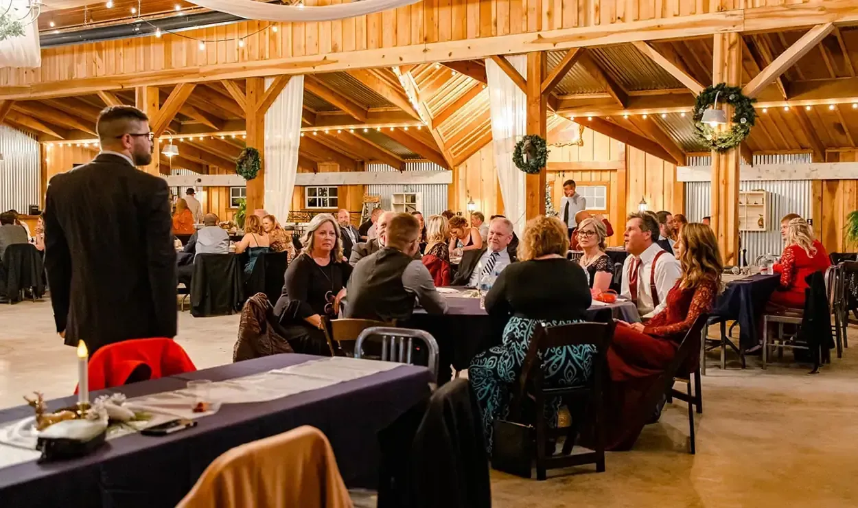 Guests seated at tables in a rustic wooden banquet hall with warm lighting