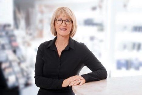Eine Frau mit Brille und schwarzem Hemd sitzt an einem Tisch.