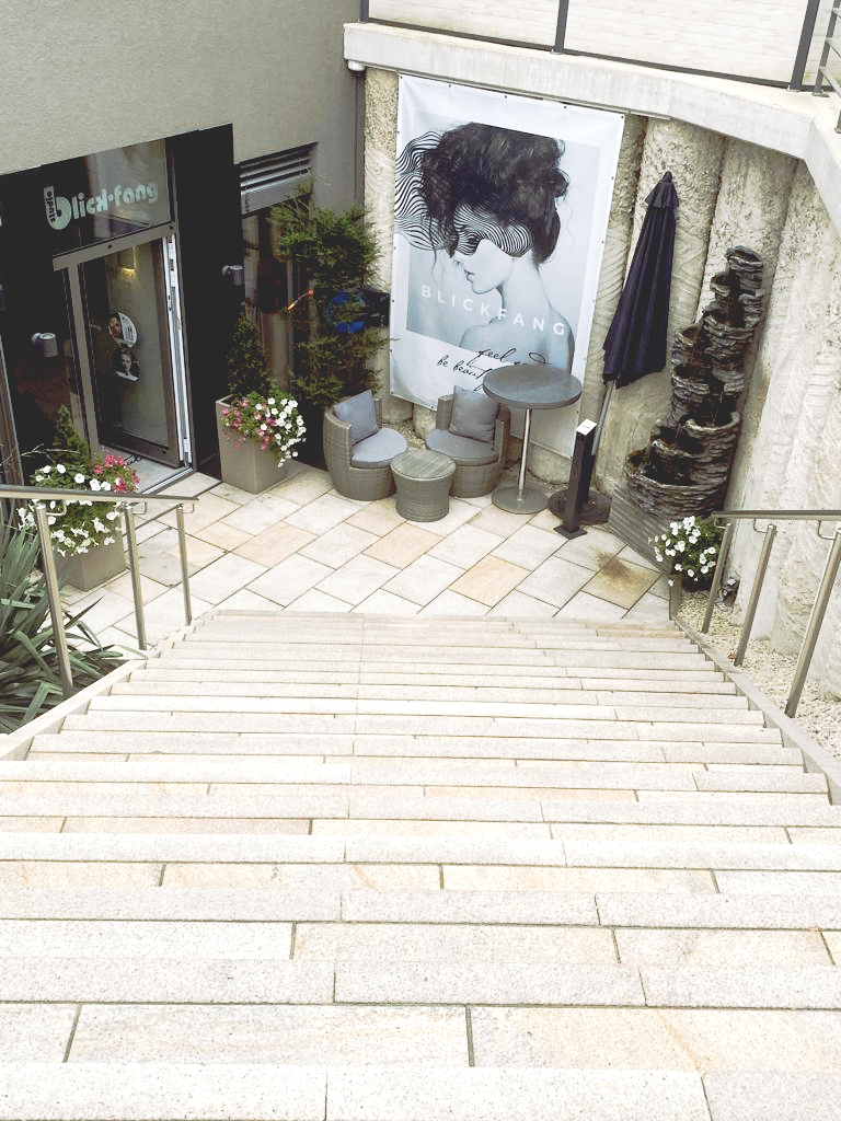 Eine Treppe führt zu einem Gebäude hinauf, an dessen Wand das Bild einer Frau hängt.