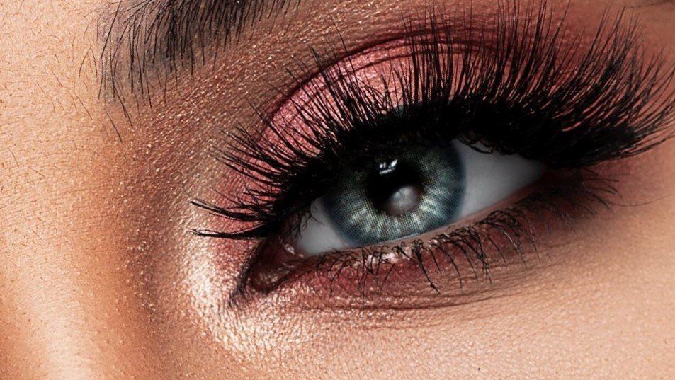 Eine Nahaufnahme des Auges einer Frau mit langen Wimpern und rosa Lidschatten.