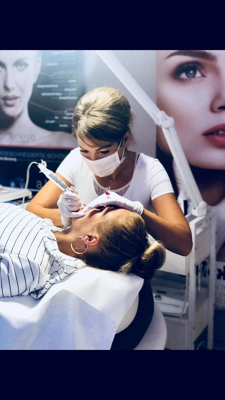 Eine Frau mit einer Maske lässt sich ein Tattoo auf das Gesicht einer Frau machen.