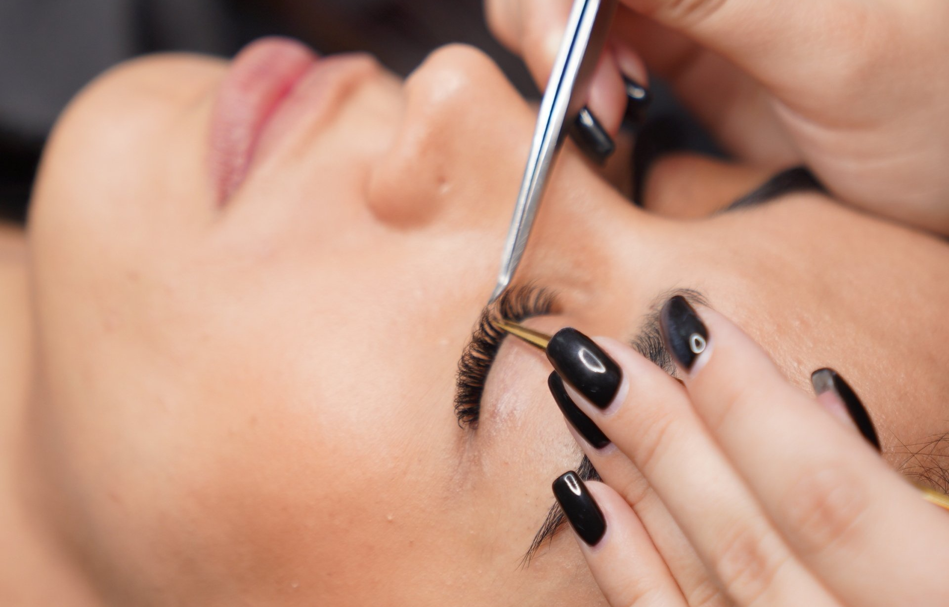 Eine Frau mit schwarzen Nägeln lässt sich die Wimpern machen.