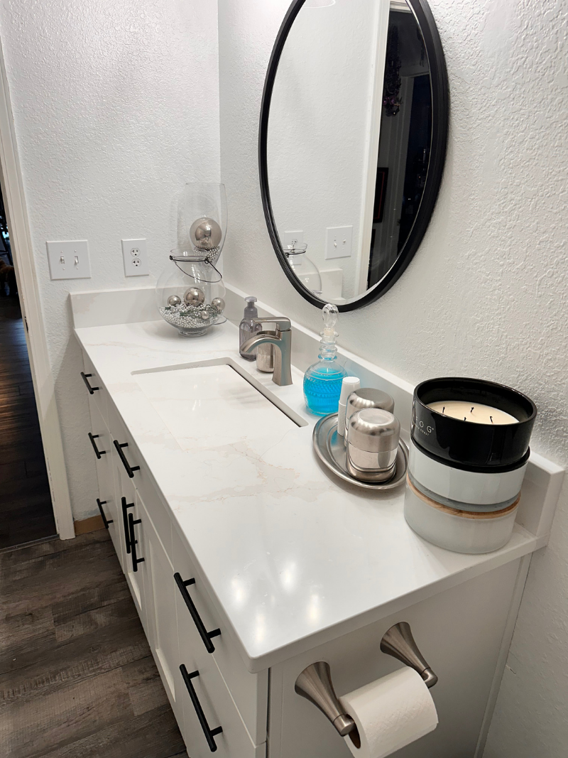 White bathroom vanity with oval mirror, sink, chrome faucet, soap dispensers, and toilet paper holder
