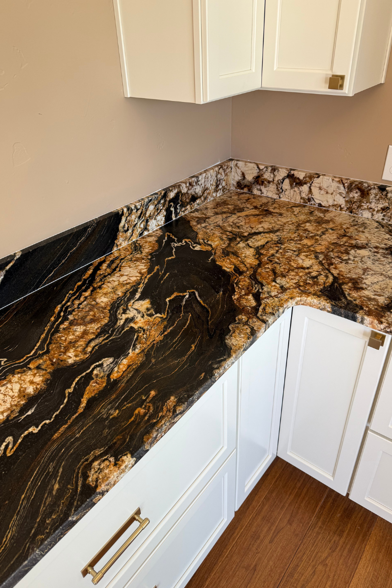 Corner kitchen countertop with black, gold, and brown marble pattern and white cabinets