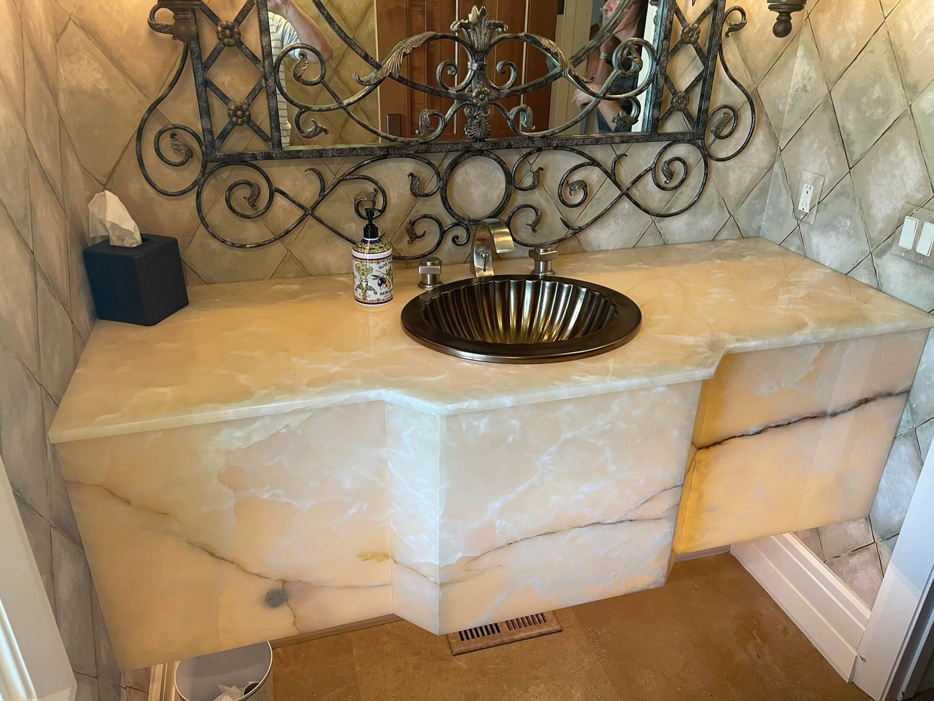 Marble bathroom vanity with round bronze sink, ornate mirror, and cream tiled backsplash