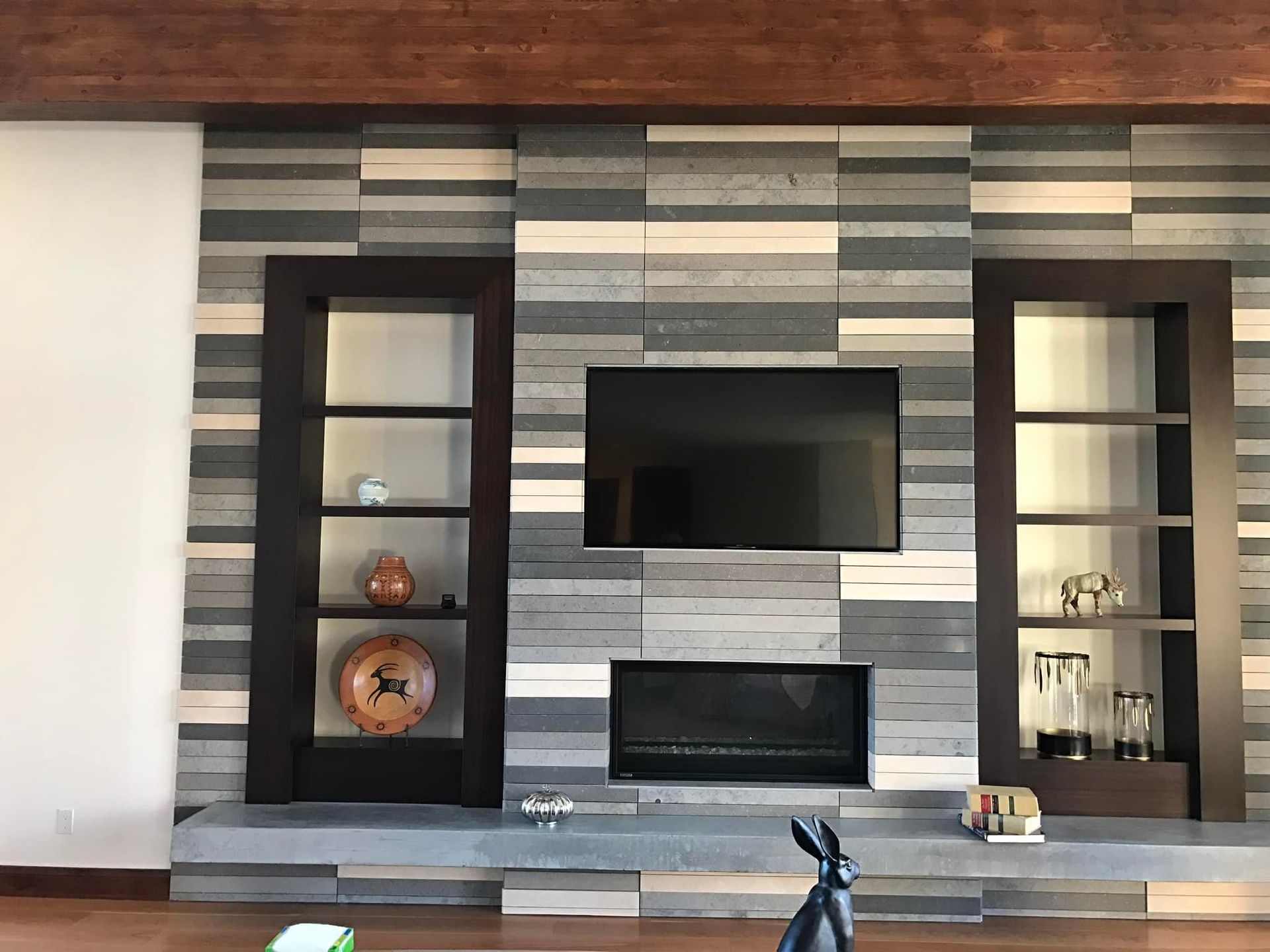 Modern living room wall with built-in shelves, striped stone fireplace, and mounted TV.