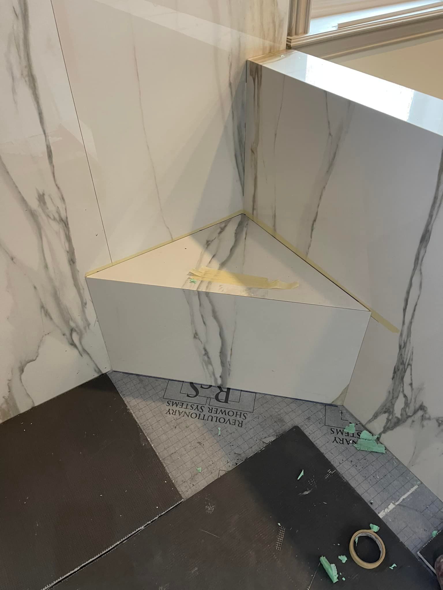 Corner of a tiled room with a triangular built-in shelf or ledge, marble-pattern walls, and a dark floor.