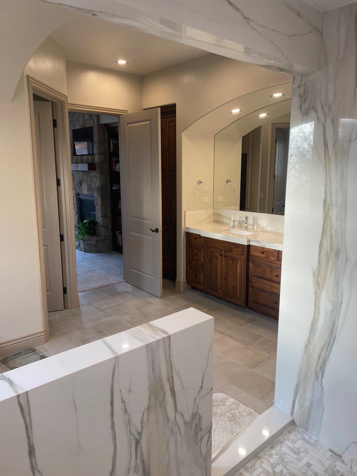 Modern bathroom with double vanity, marble counters, large mirror, and tiled walk-in shower entrance