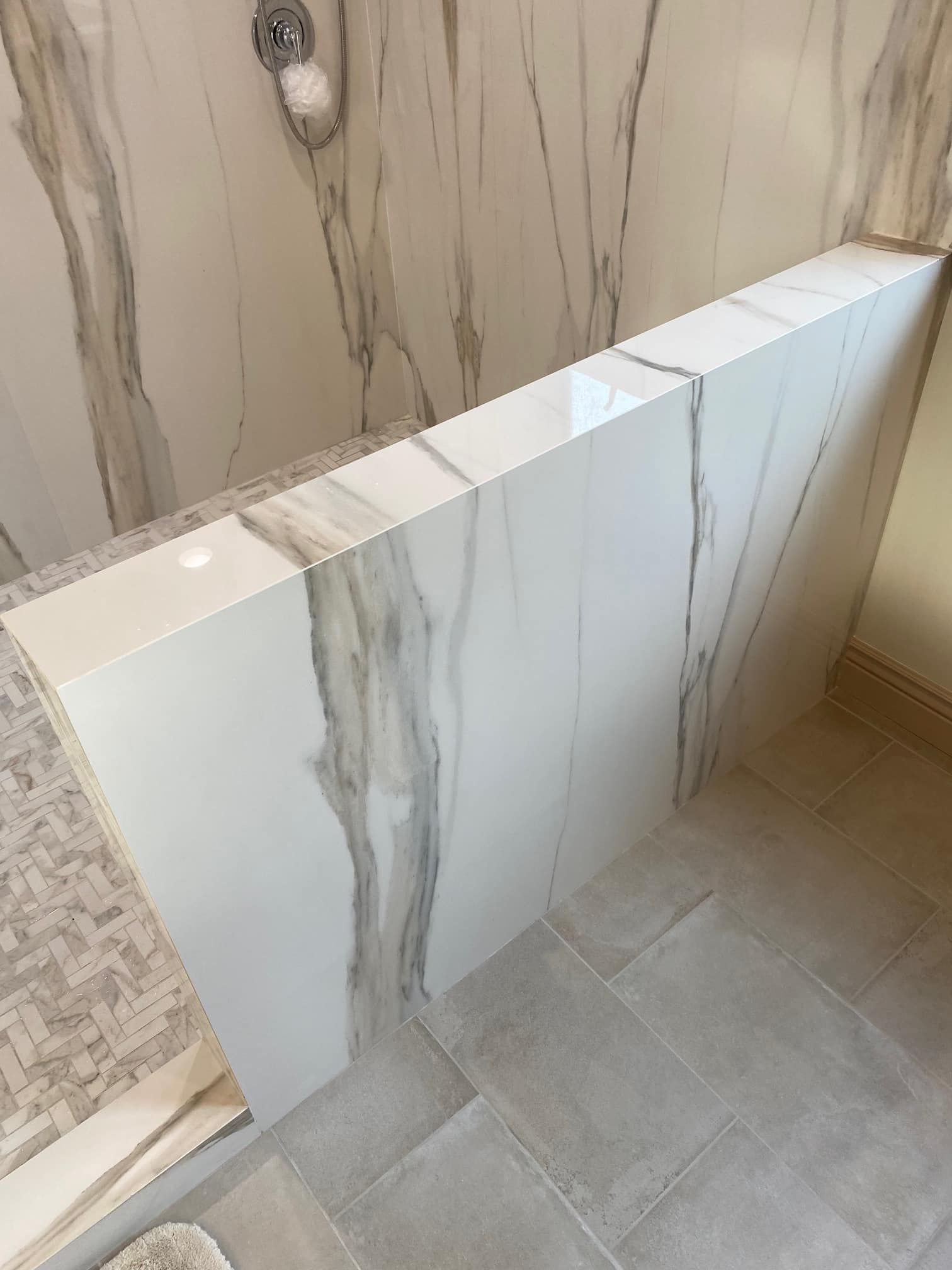White tiled shower bench and beige marble wall in a bathroom, viewed from above.