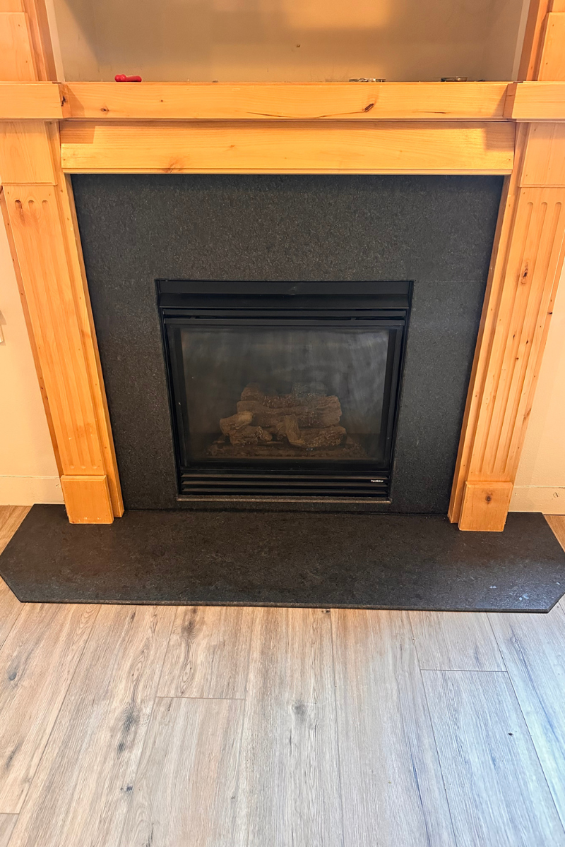 Black fireplace insert framed by unfinished wood, with a dark hearth and light floor in front.