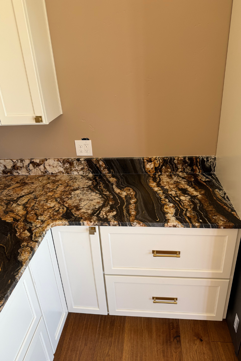 Granite bathroom vanity corner with white cabinets and drawers beneath a tan wall.