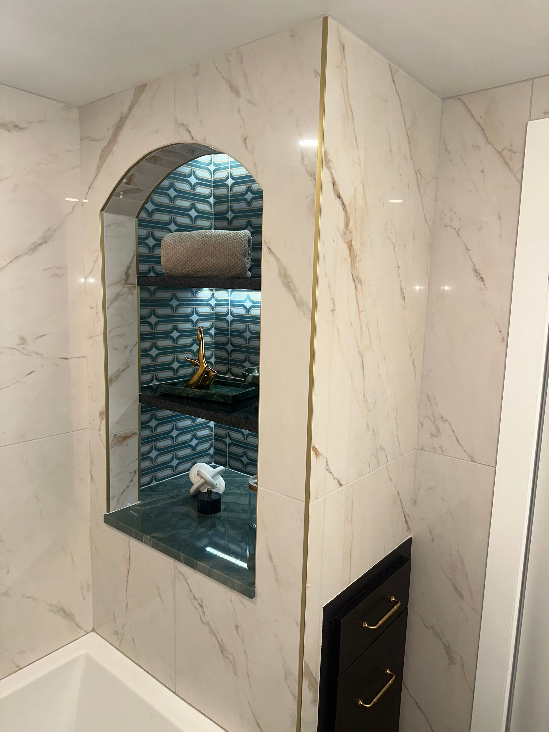 Built-in marble shower niche with arched opening, dark tiled back wall, and gold faucet fixture