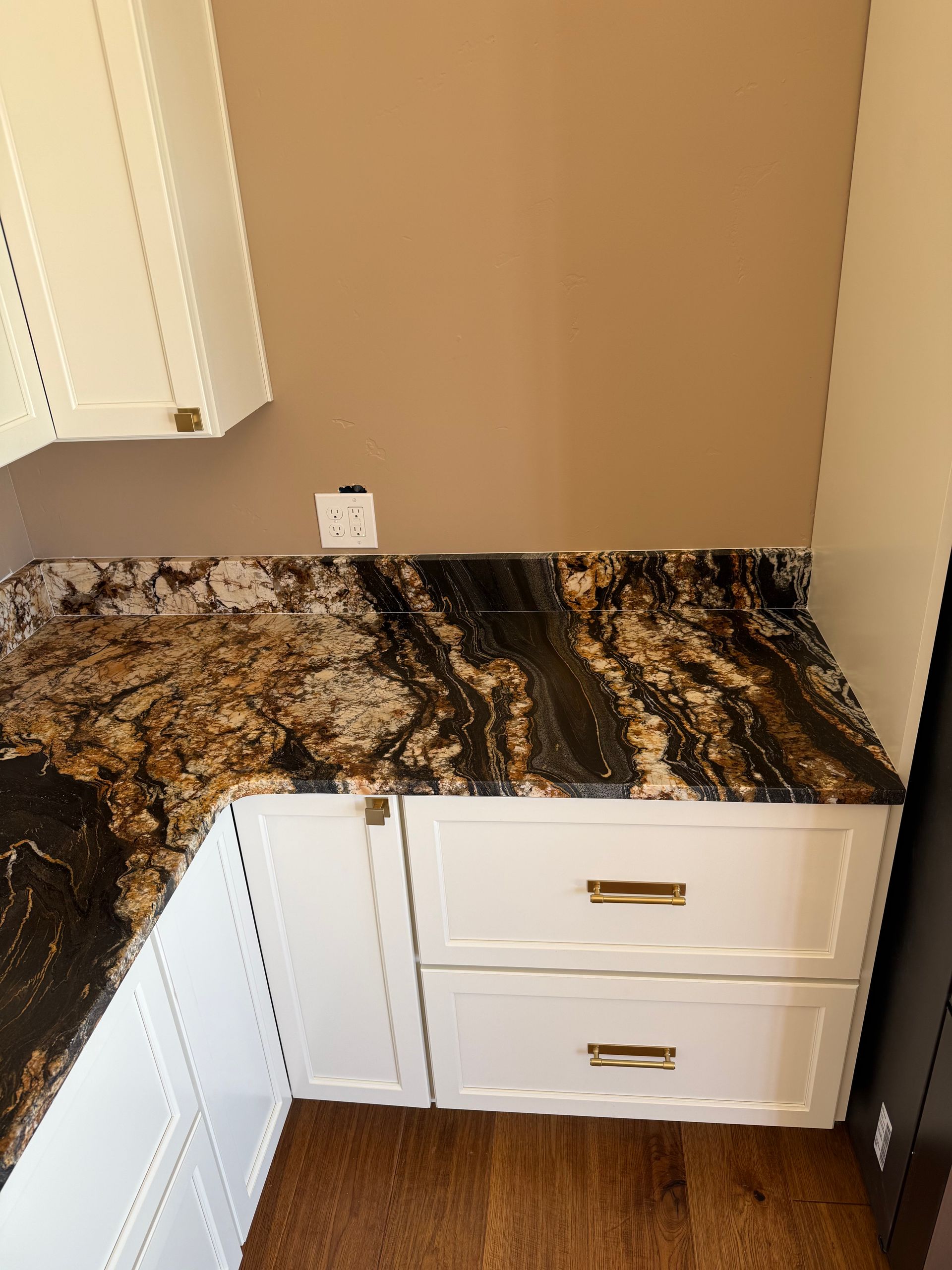 Corner kitchen cabinet with black-and-gold granite countertop, white drawers, and beige walls