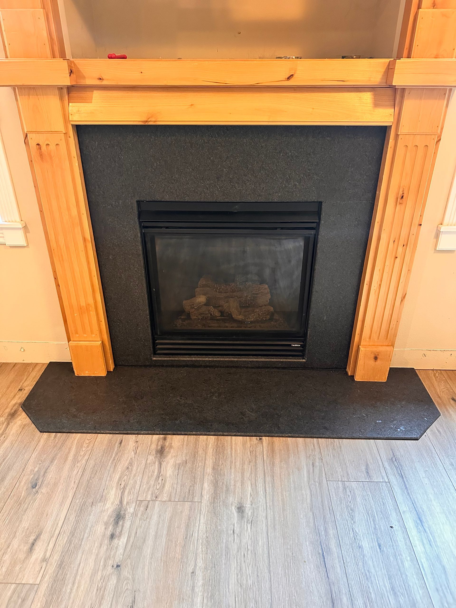 Fireplace with dark surround set into a wood-paneled wall above a black hearth mat.