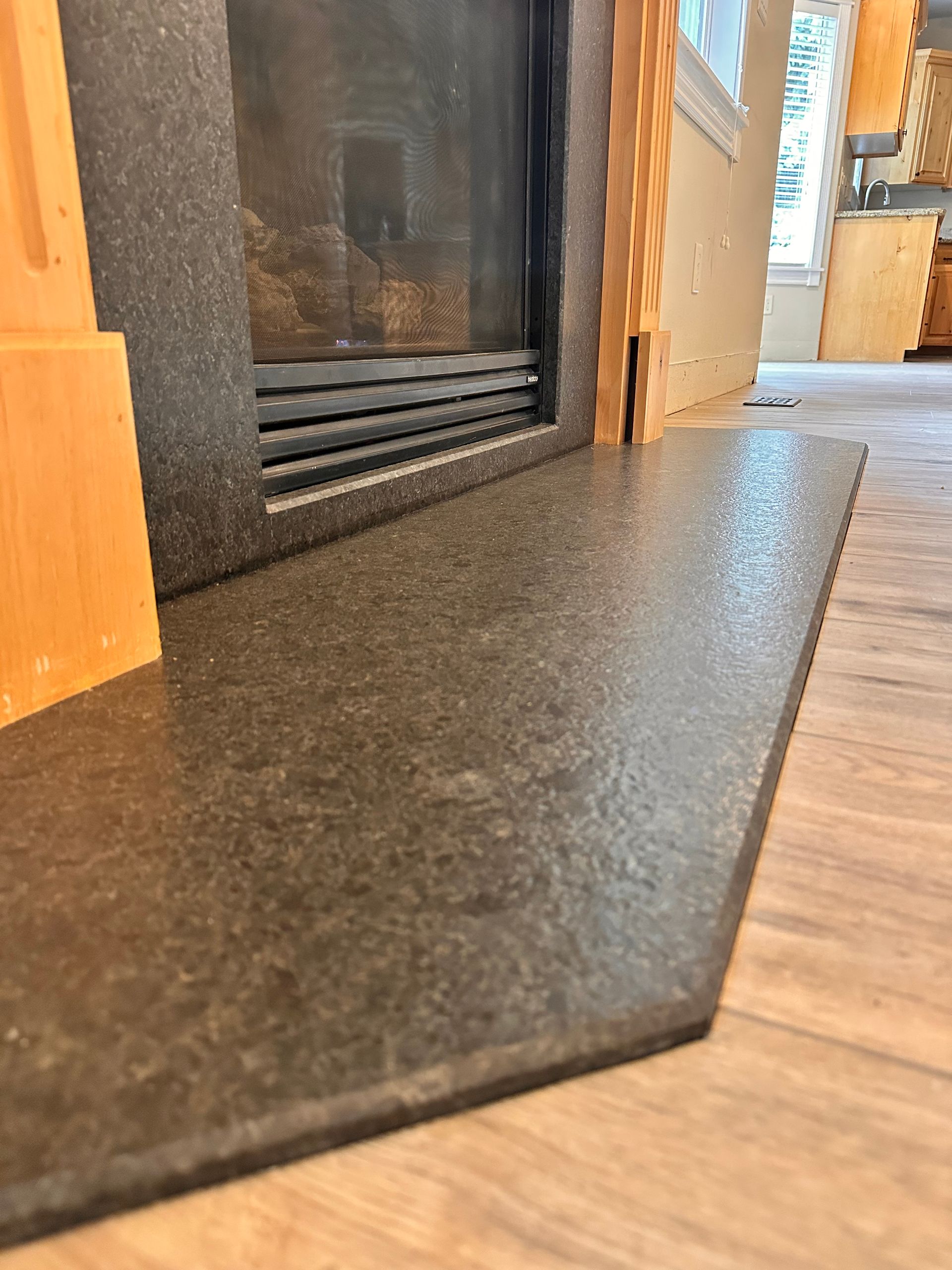 Close-up of a black stone fireplace hearth with orange wood paneling in a room