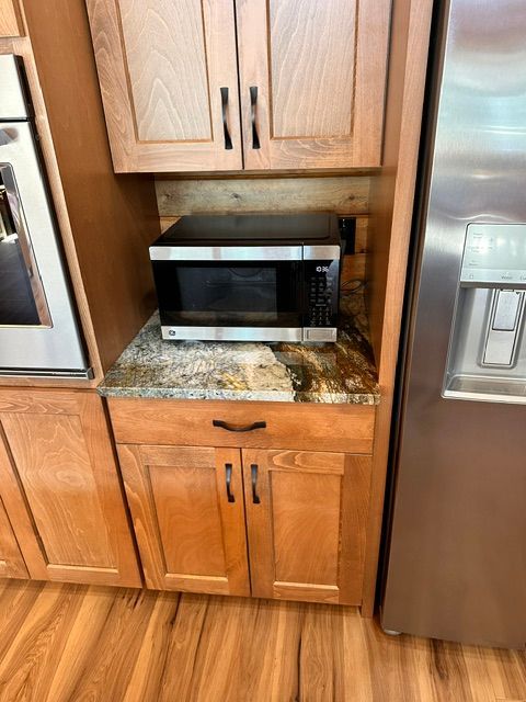 Kitchen cabinet nook with a black microwave on a granite counter beside a stainless steel refrigerator.