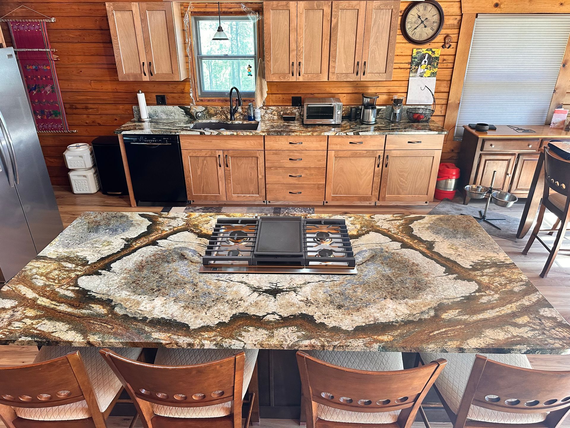 Rustic cabin kitchen and dining area with wood cabinets, stone counter, patterned rug, and wooden chairs