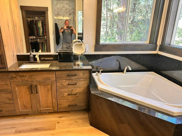 Bathroom with wood vanity, large mirror, and white corner tub beside a window.