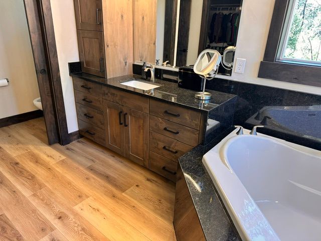 Spacious bathroom with wood vanity, dark granite countertop, white tub, and window light