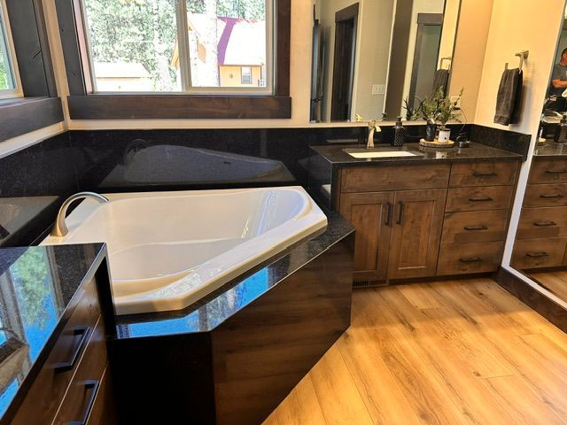 Modern bathroom with corner soaking tub, dark wood vanity, black counters, and wood-look tile floor