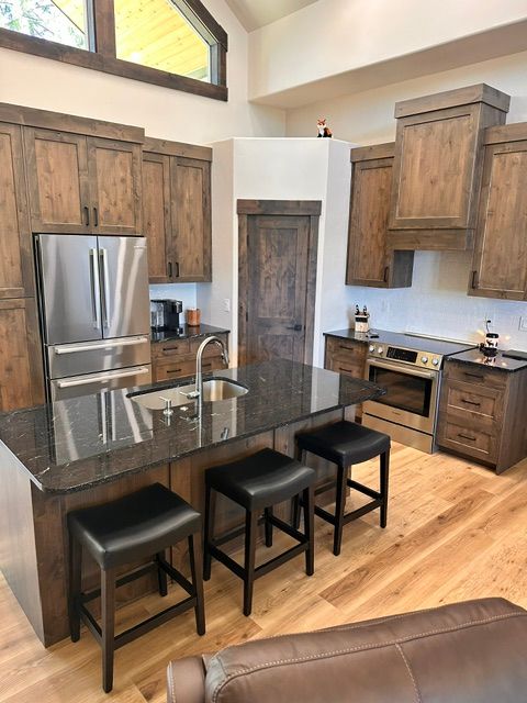Modern kitchen with stainless fridge, dark island with three stools, and wood cabinets