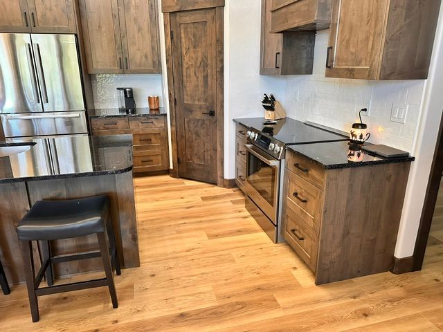 Modern kitchen with wood floors, stainless fridge, island stool, and dark countertops